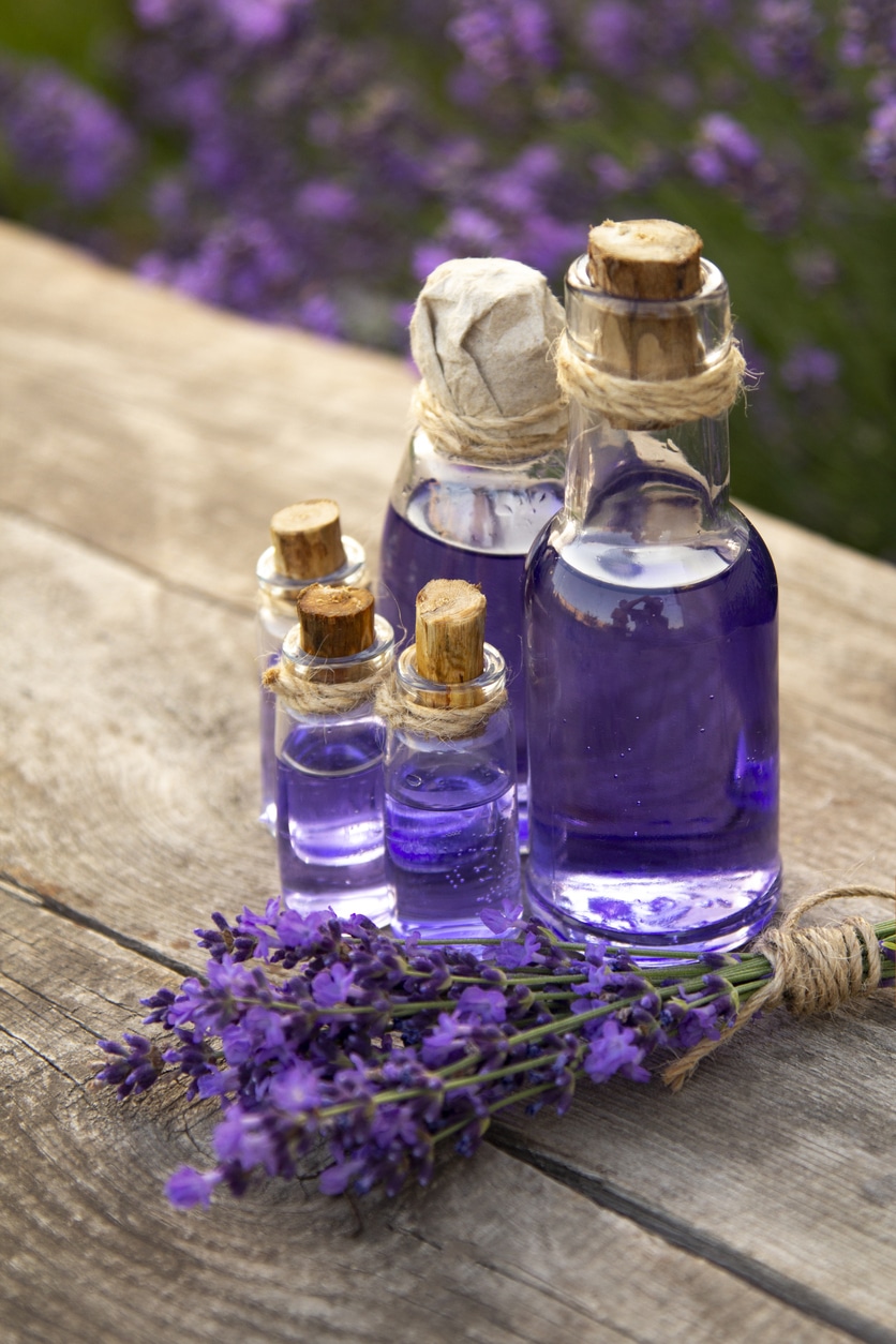 Lavender Essential oil bottle on wood table and flowers field background